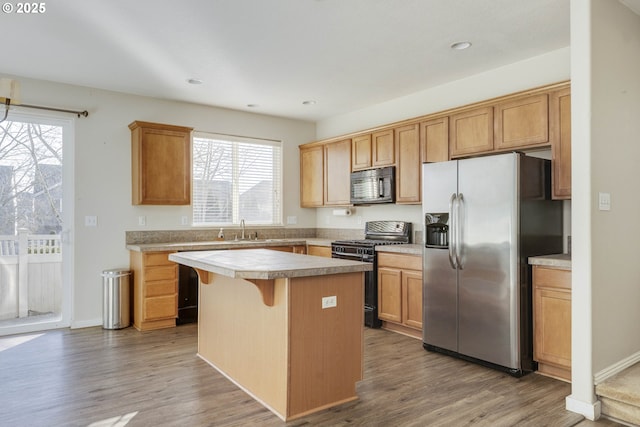 kitchen with hardwood / wood-style floors, sink, a kitchen breakfast bar, a center island, and black appliances