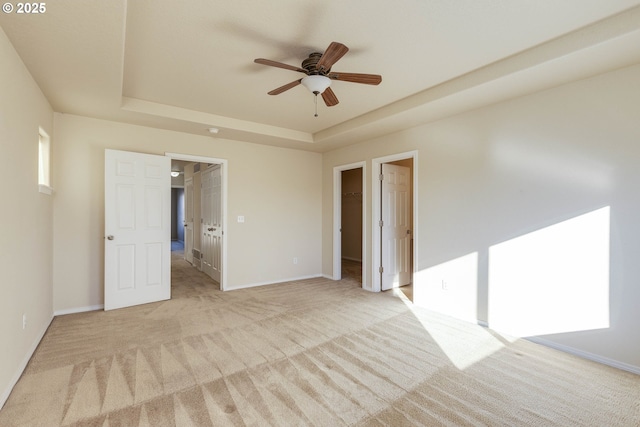 empty room with light colored carpet, a raised ceiling, and ceiling fan