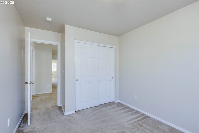 unfurnished bedroom featuring light carpet, a closet, and a textured ceiling