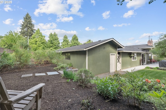 view of side of home with a patio, a chimney, and a shingled roof