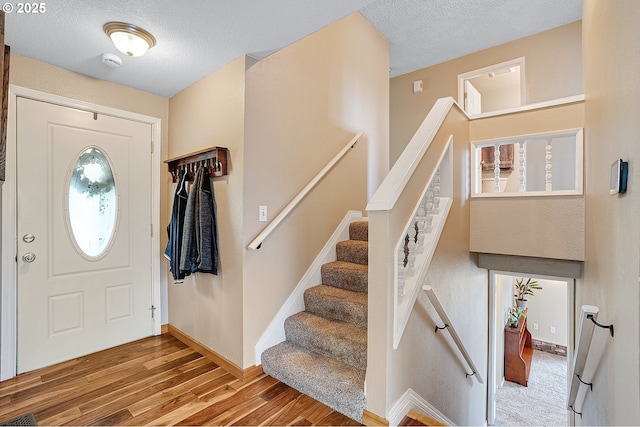 foyer with wood finished floors, a textured ceiling, baseboards, and stairs