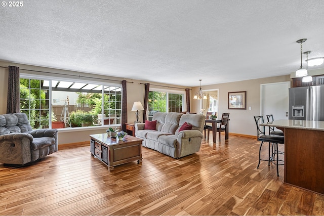 living room with a textured ceiling, a chandelier, plenty of natural light, wood finished floors, and baseboards