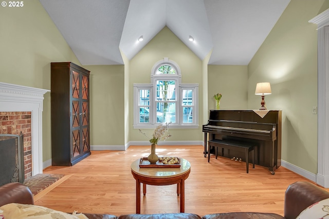 living room featuring light wood-style floors, baseboards, a fireplace, and lofted ceiling
