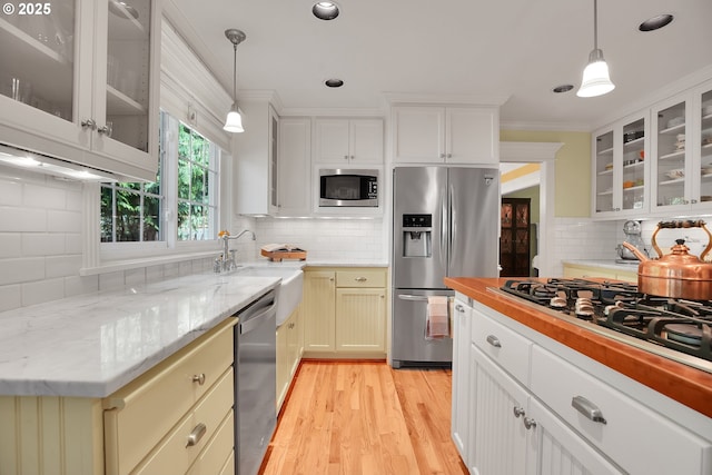 kitchen with pendant lighting, appliances with stainless steel finishes, tasteful backsplash, light wood-type flooring, and a sink