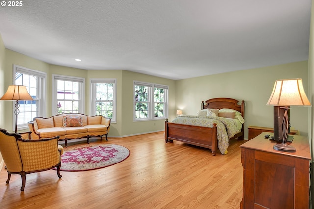 bedroom with baseboards, a textured ceiling, light wood-style flooring, and multiple windows