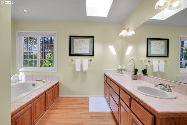 full bathroom featuring a skylight, baseboards, a sink, and wood finished floors