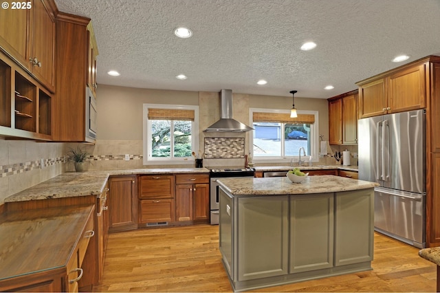 kitchen with a healthy amount of sunlight, wall chimney range hood, stainless steel appliances, and light wood-style floors