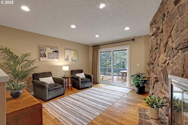 living room featuring a textured ceiling, a stone fireplace, wood finished floors, and recessed lighting