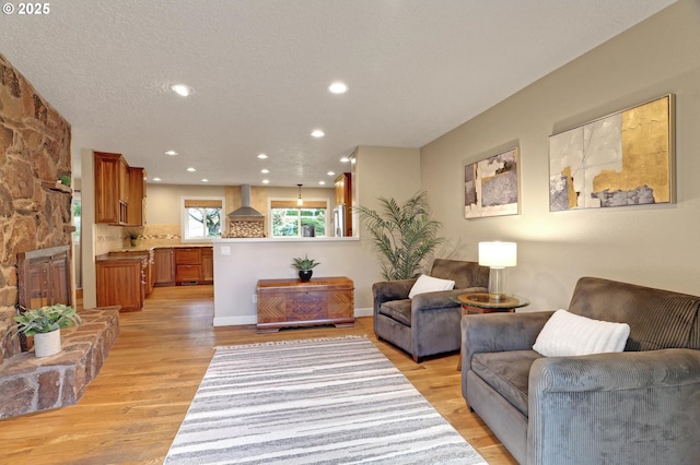 living area featuring a textured ceiling, light wood-type flooring, baseboards, and recessed lighting