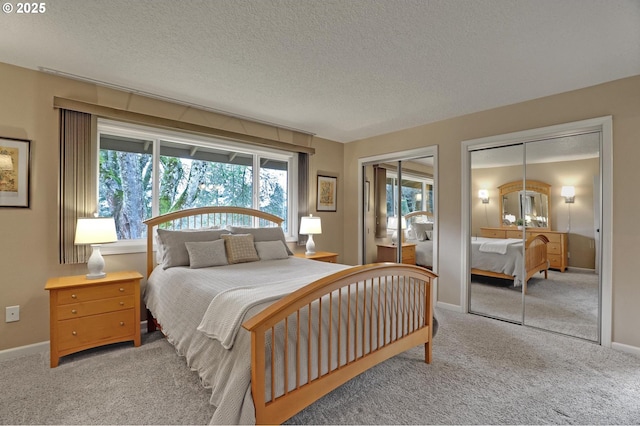 carpeted bedroom with a textured ceiling, two closets, and baseboards