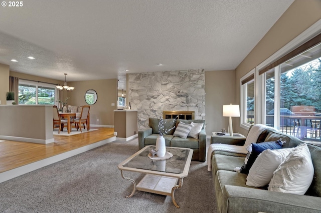 living room with a textured ceiling, a chandelier, a stone fireplace, baseboards, and carpet