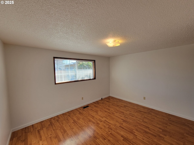 empty room featuring light wood-style floors, visible vents, a textured ceiling, and baseboards