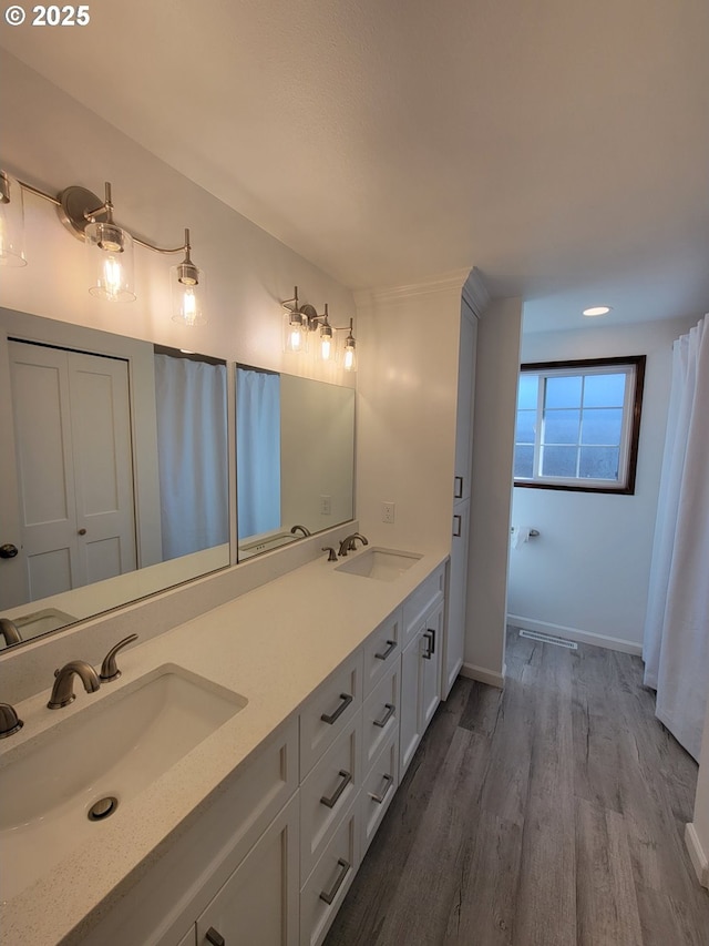 full bathroom with double vanity, a sink, baseboards, and wood finished floors