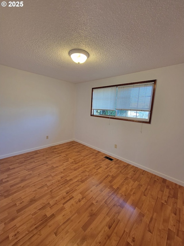 spare room featuring light wood-type flooring, visible vents, a textured ceiling, and baseboards