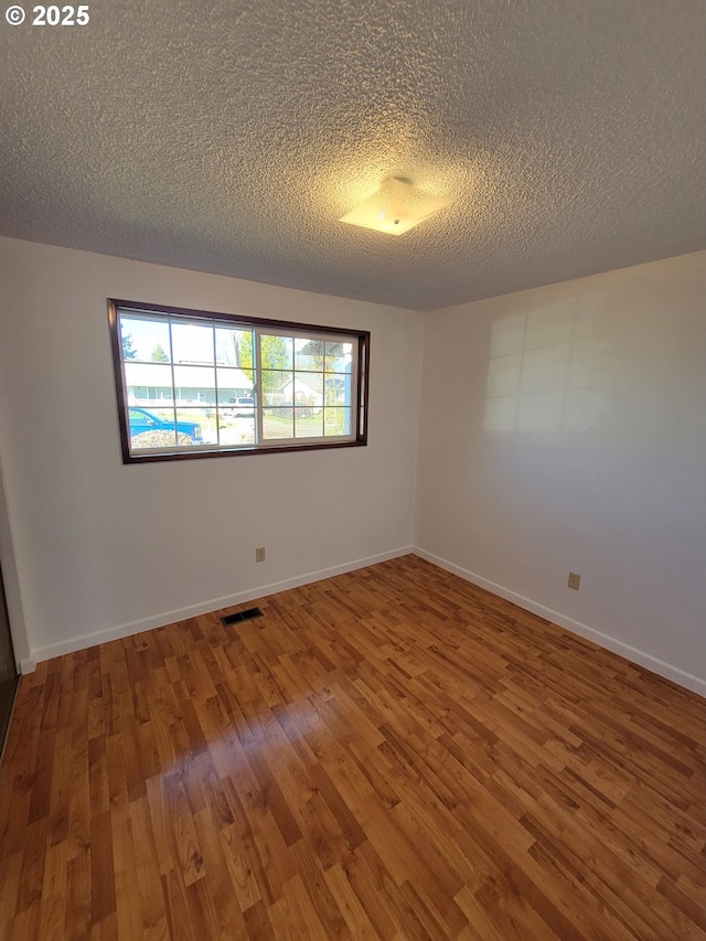 unfurnished room with visible vents, a textured ceiling, baseboards, and wood finished floors