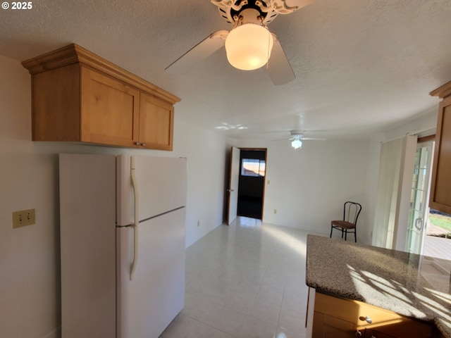 kitchen featuring dark stone counters, a ceiling fan, freestanding refrigerator, and a healthy amount of sunlight