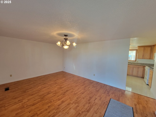 unfurnished room featuring light wood-style floors, visible vents, a notable chandelier, and a textured ceiling