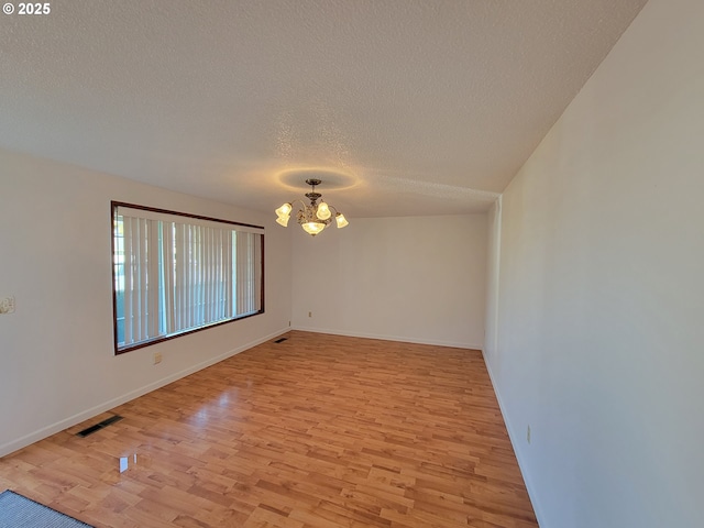 unfurnished room with light wood finished floors, visible vents, a textured ceiling, a chandelier, and baseboards