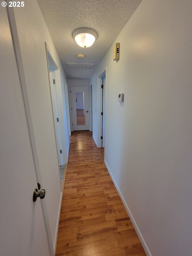 hall with light wood-type flooring, a textured ceiling, and baseboards