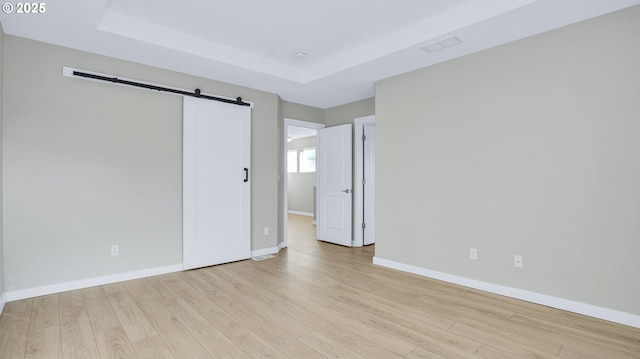 unfurnished room with a barn door, a raised ceiling, light wood-style flooring, and baseboards