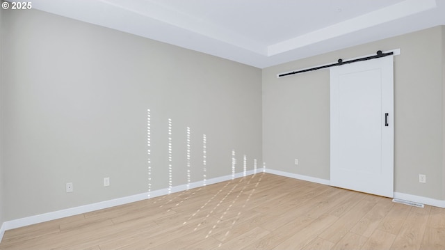 unfurnished room featuring light wood-type flooring, visible vents, baseboards, and a barn door