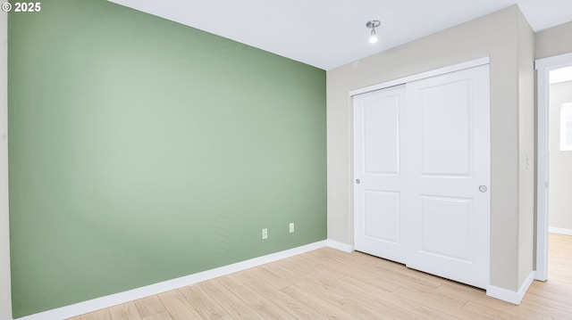 unfurnished bedroom featuring a closet, light wood-style flooring, and baseboards