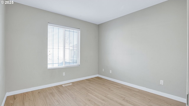 spare room with light wood finished floors, visible vents, and baseboards