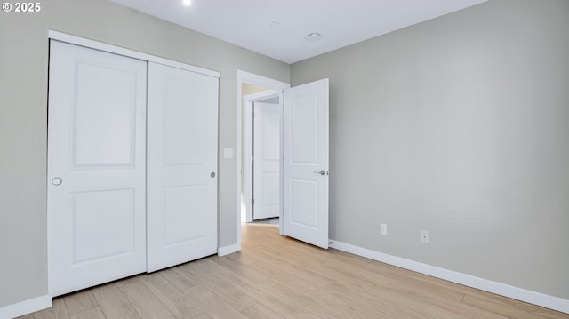 unfurnished bedroom featuring light wood-type flooring, baseboards, and a closet