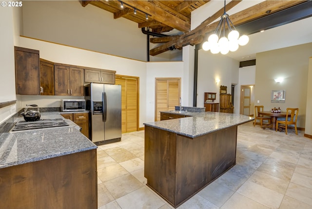 kitchen with appliances with stainless steel finishes, dark stone countertops, beamed ceiling, decorative light fixtures, and a high ceiling