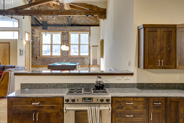 kitchen with gas range, dark brown cabinets, open floor plan, and dark stone countertops