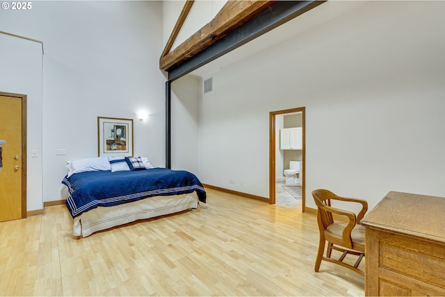 bedroom featuring ensuite bathroom, light wood-style flooring, visible vents, a towering ceiling, and baseboards