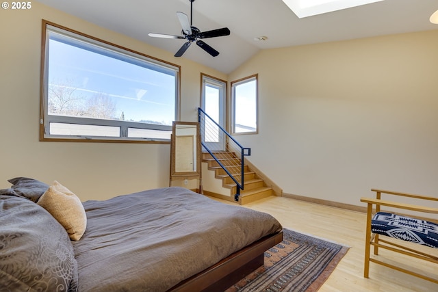 bedroom with vaulted ceiling with skylight, baseboards, ceiling fan, and wood finished floors