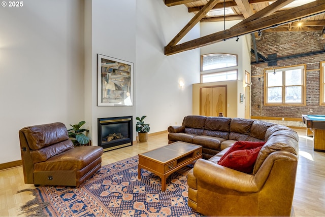 living area featuring high vaulted ceiling, a glass covered fireplace, beamed ceiling, and wood finished floors