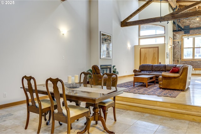 dining area with a towering ceiling, light tile patterned floors, baseboards, and a glass covered fireplace