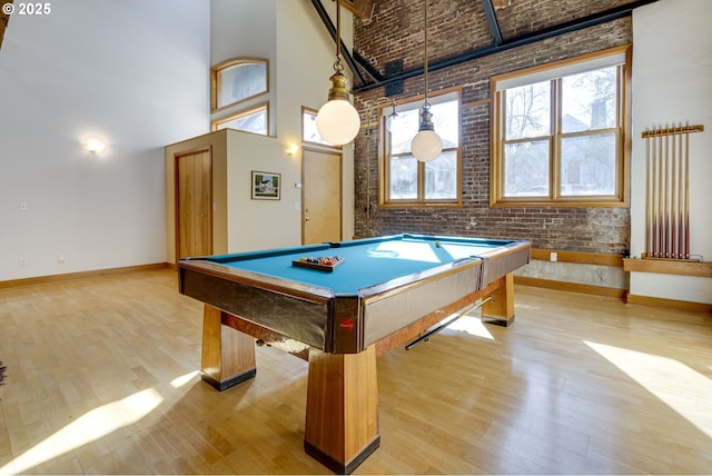 rec room with billiards, baseboards, a towering ceiling, brick wall, and light wood-style flooring