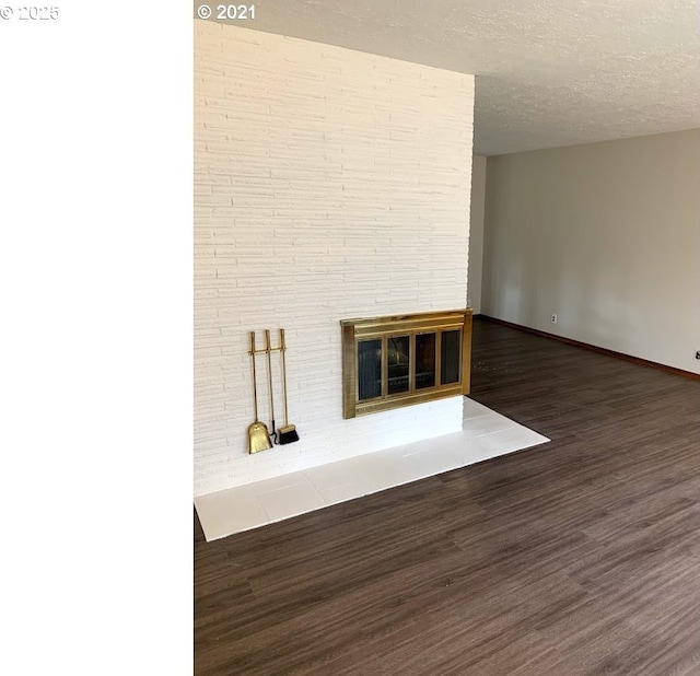 unfurnished living room with a brick fireplace, a textured ceiling, and dark hardwood / wood-style flooring