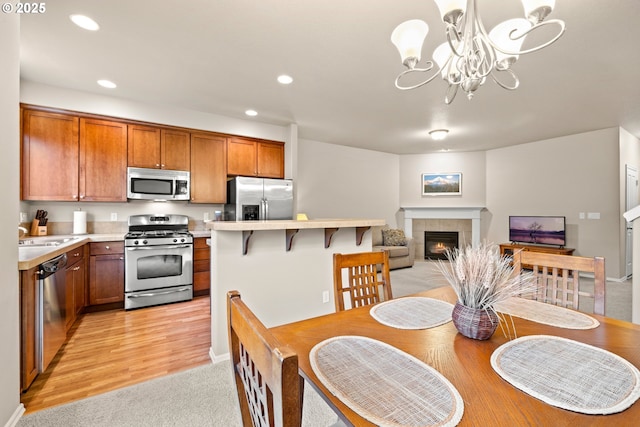 dining space featuring an inviting chandelier, light wood finished floors, a tiled fireplace, and recessed lighting