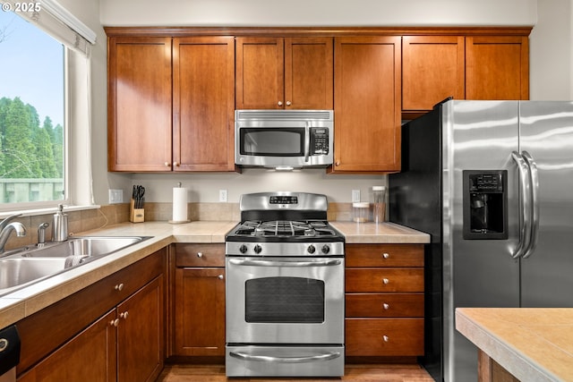 kitchen featuring appliances with stainless steel finishes, brown cabinetry, light countertops, and a sink