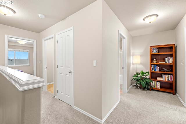 corridor with light colored carpet, a textured ceiling, and baseboards