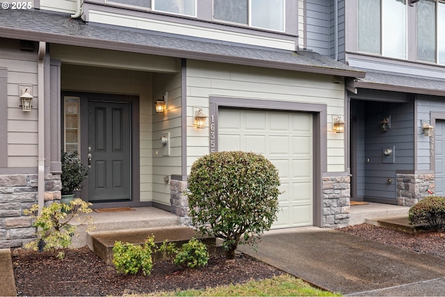 doorway to property with a garage, stone siding, and roof with shingles