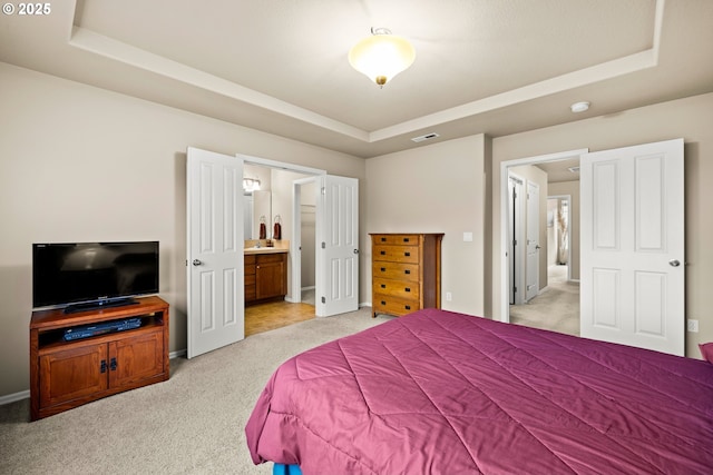 bedroom featuring visible vents, baseboards, light colored carpet, ensuite bath, and a tray ceiling