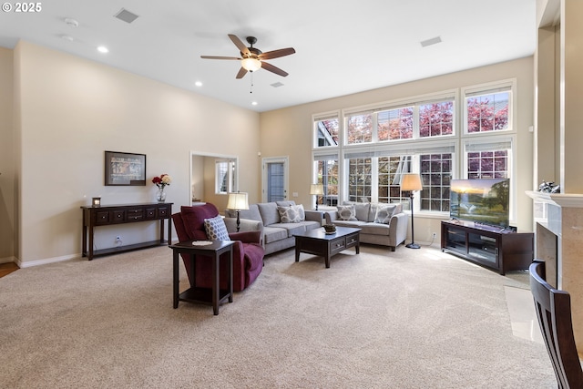 living area with a ceiling fan, visible vents, baseboards, a high ceiling, and light carpet