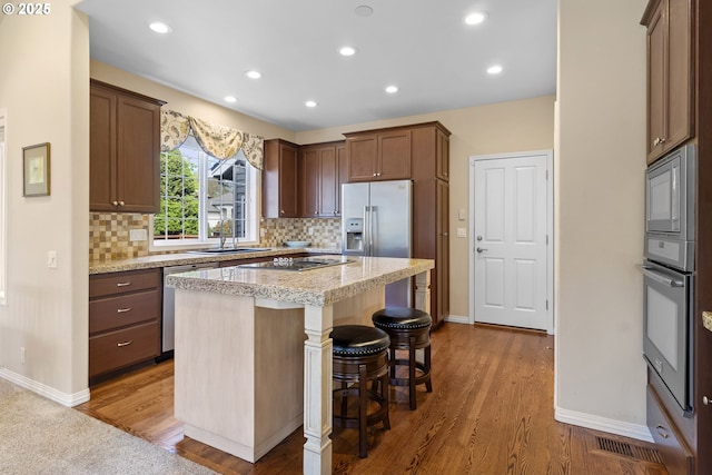 kitchen with a kitchen breakfast bar, backsplash, appliances with stainless steel finishes, wood finished floors, and a sink