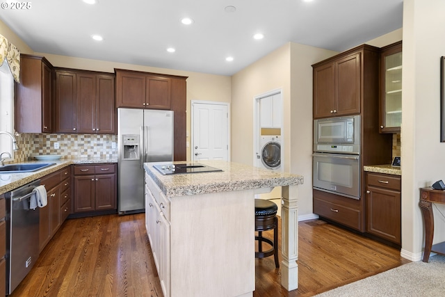kitchen with a kitchen island, appliances with stainless steel finishes, a sink, washer / dryer, and dark wood-type flooring