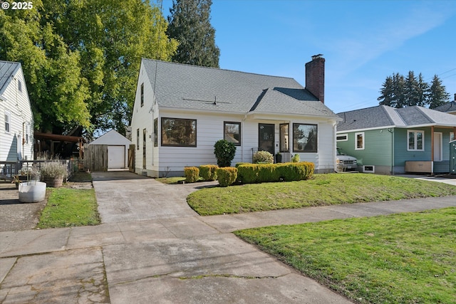 view of front of house featuring an outbuilding, a detached garage, a chimney, concrete driveway, and a front lawn