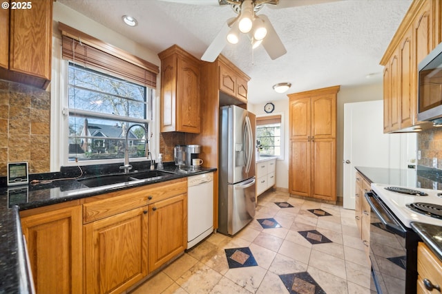 kitchen with a textured ceiling, a sink, appliances with stainless steel finishes, backsplash, and dark stone countertops