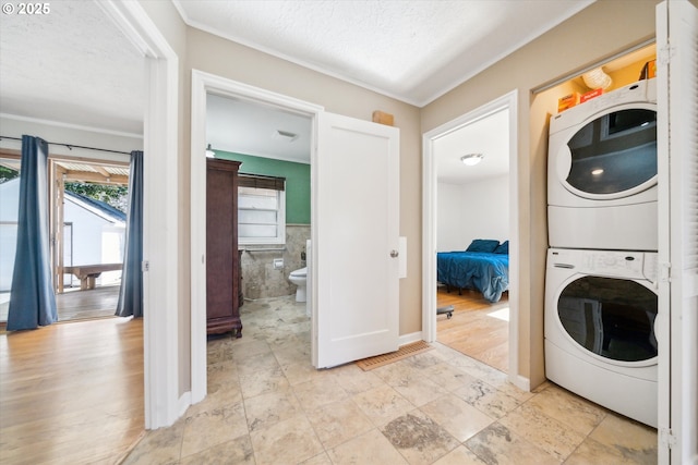 clothes washing area featuring a textured ceiling, a wainscoted wall, laundry area, stacked washing maching and dryer, and light wood finished floors