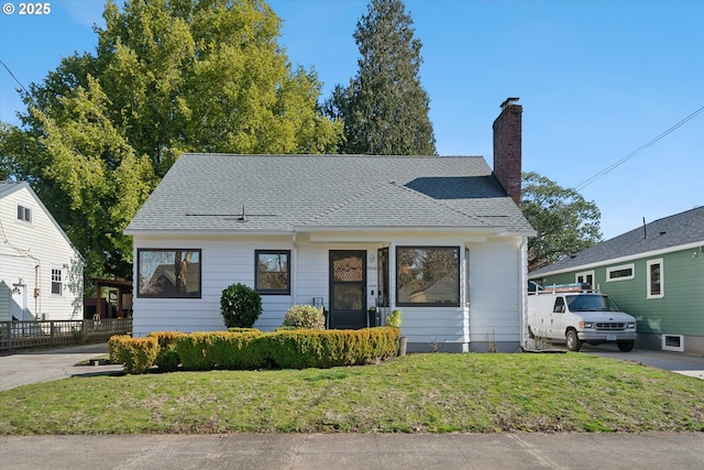 bungalow-style house with a front yard, roof with shingles, and a chimney