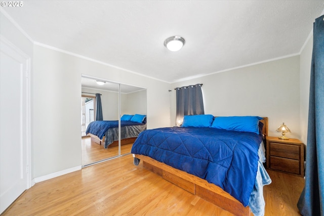 bedroom with a closet, crown molding, baseboards, and wood finished floors