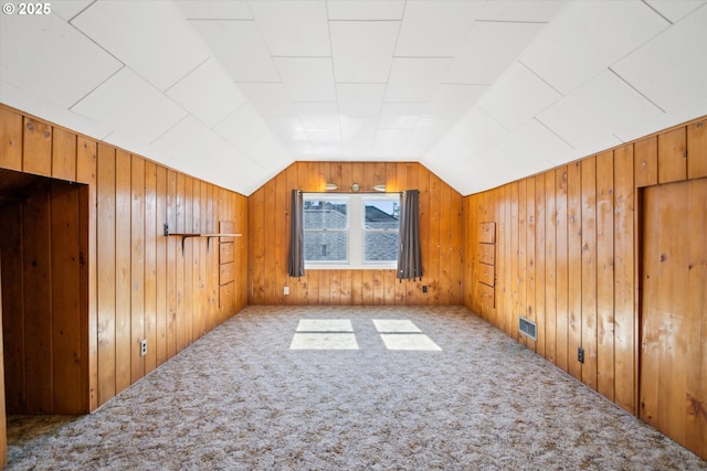 additional living space with vaulted ceiling, carpet floors, wood walls, and visible vents